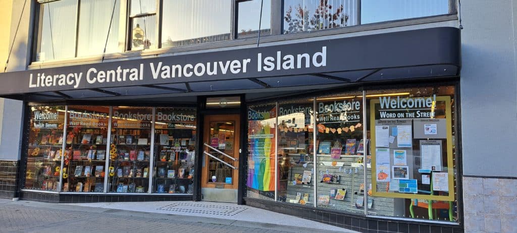 A rainbow flag, books and posters in the windows of a store front.